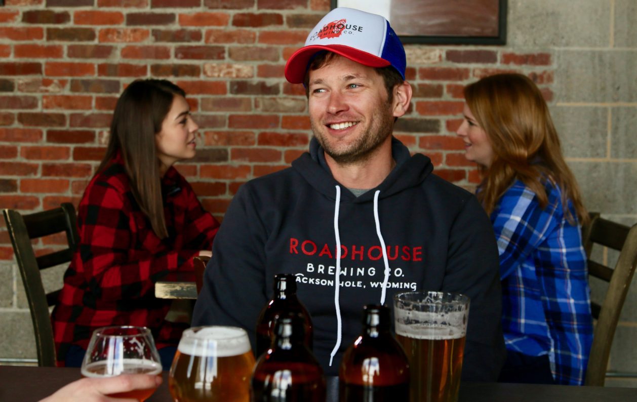 A man wearing a hat sitting at a table with several beers.