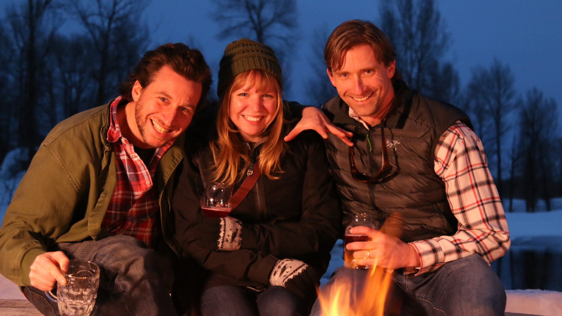 Three people sitting around a fire at night.