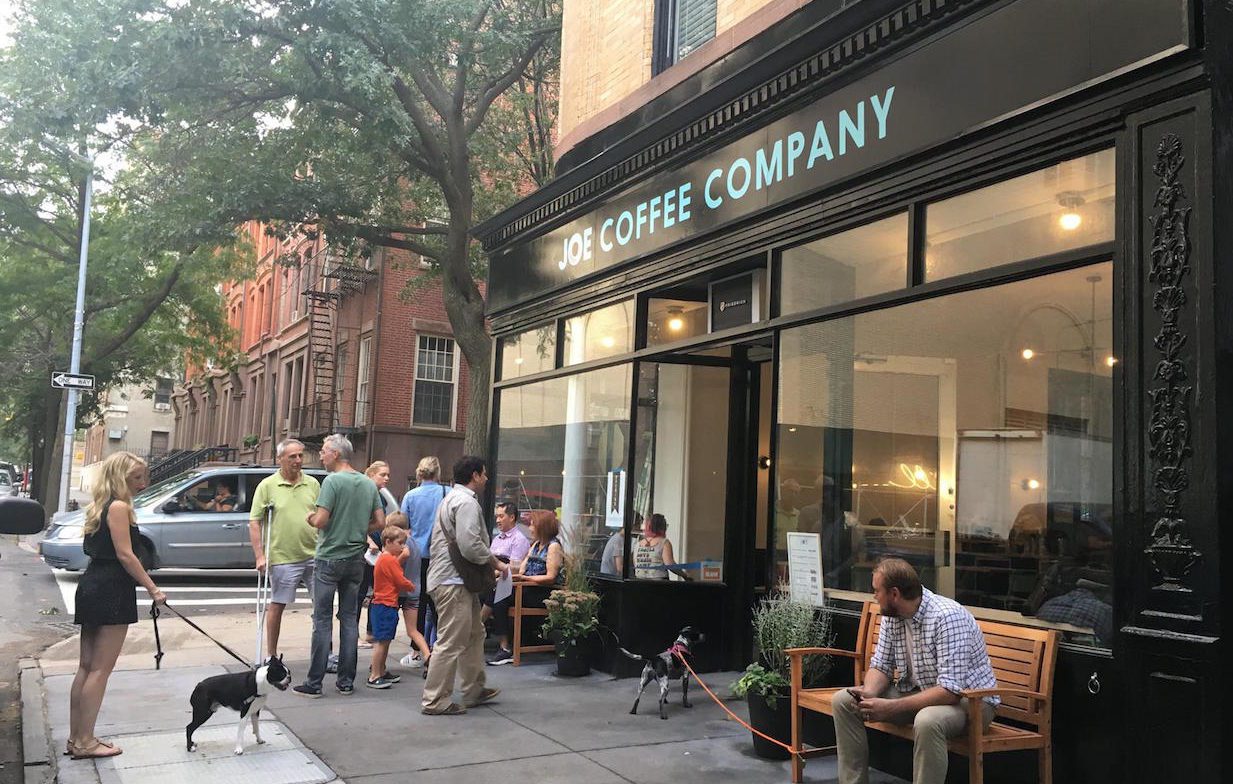 A group of people standing outside of a coffee shop.